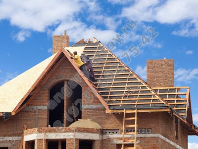 House under construction. Workesr installing fibreboard on the roof